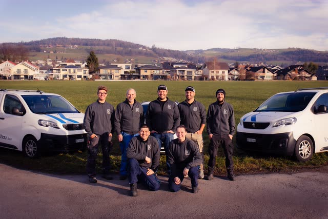 Das Team der K-Metallbau GmbH vor den beiden Firmenfahrzeugen mit Blick über Felder und Wohnhäuser