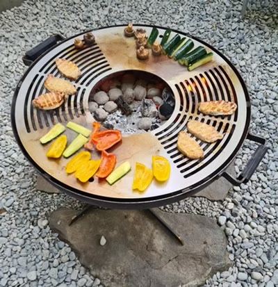 Feuerschale im Betrieb mit Grillgut auf dem ringförmigen Rost und Glut in der Mitte