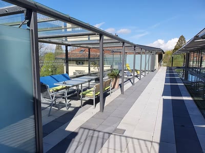 Terrassenüberdachung aus Metall und Glas mit seitlichen Windschutzelementen